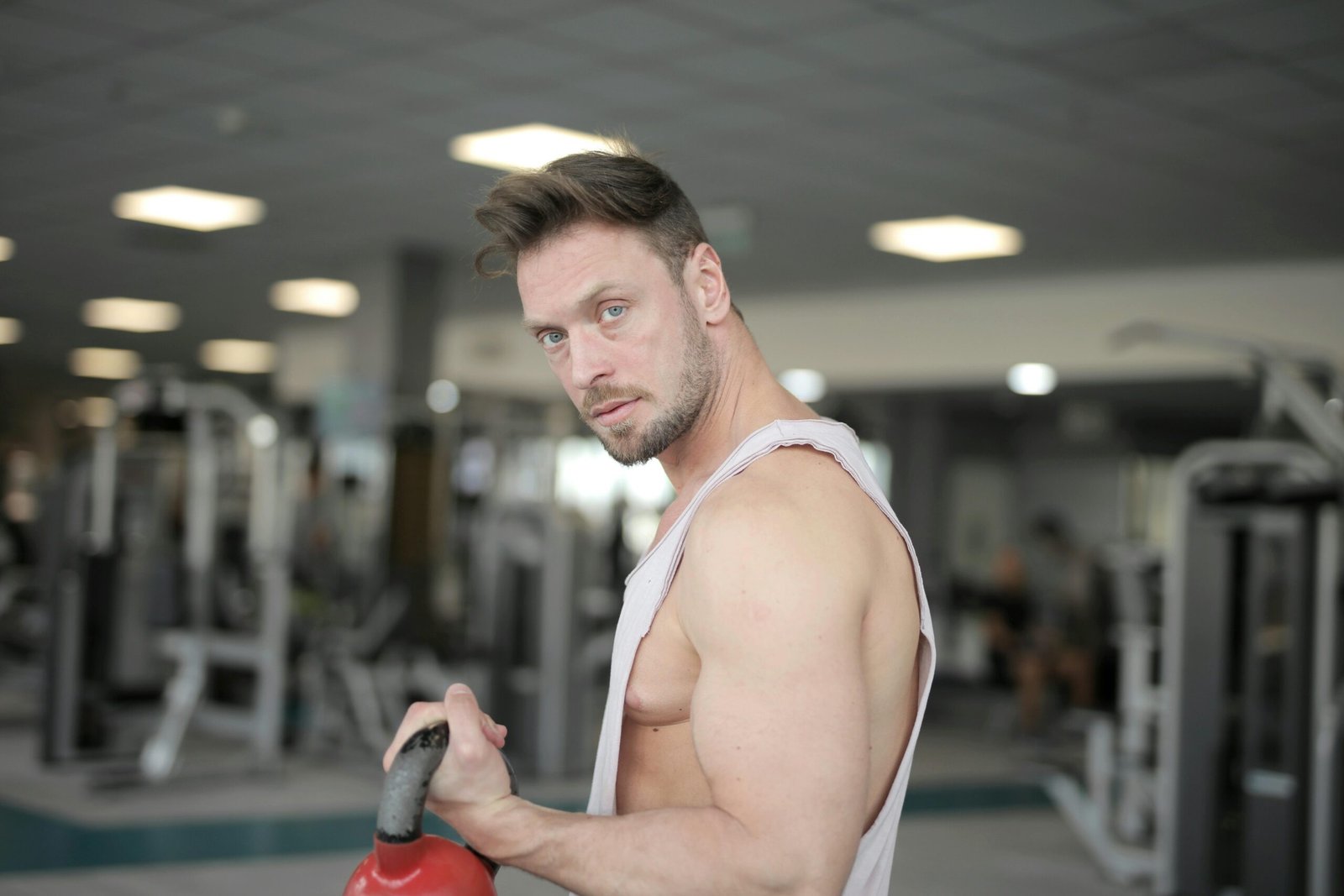 A muscular man in a gym environment working out with a kettlebell, showcasing strength and determination.